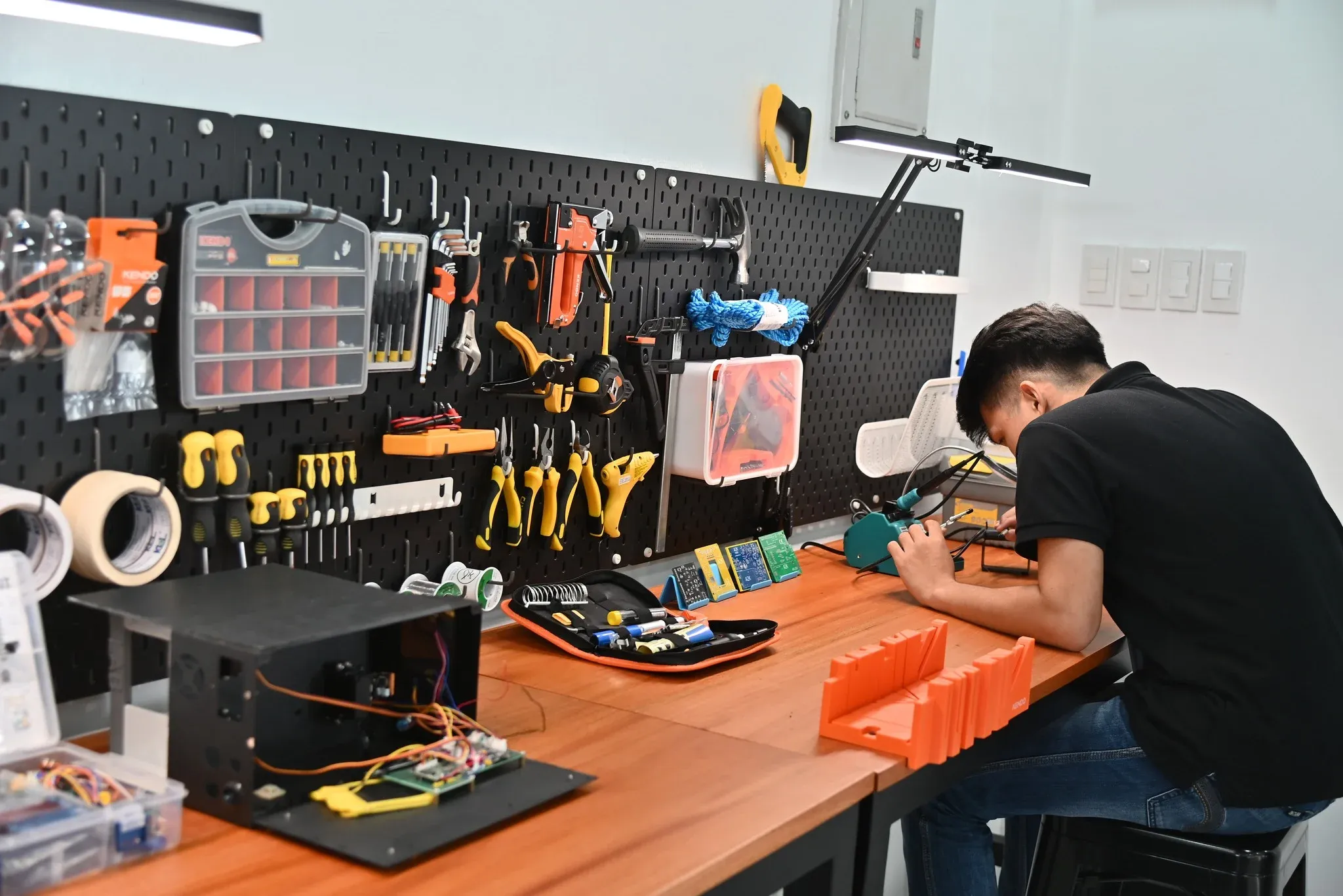 An A2K engineer assembling electronics at a workbench lined with tools